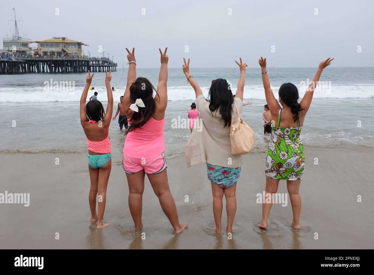 Four Asian Filipino young women raising their hands on the beach in Pacific Park, Santa Monica, Los Angeles, California, USA, United States Stock Photo