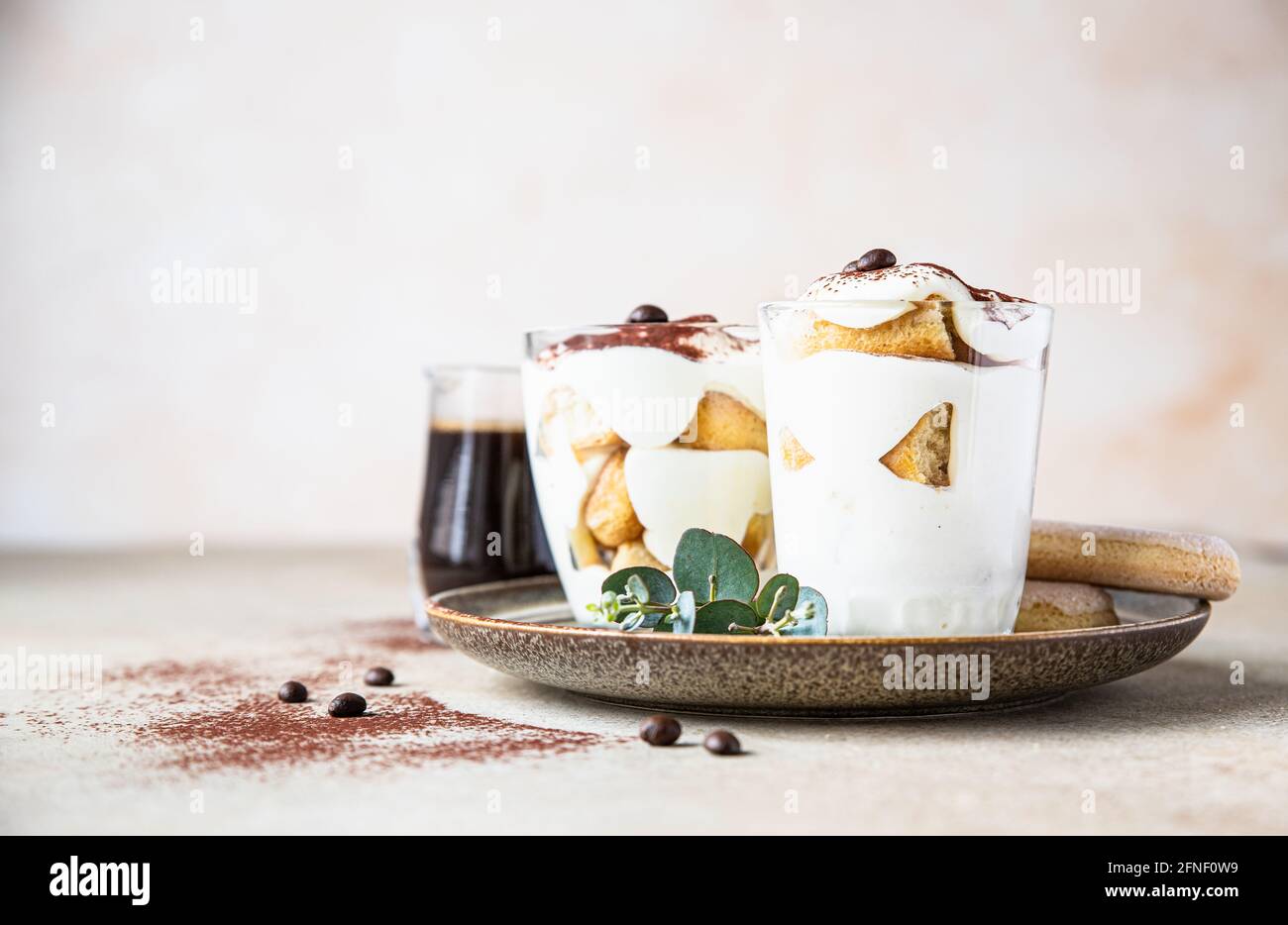 Traditional Italian dessert tiramisu in glass, light stone background