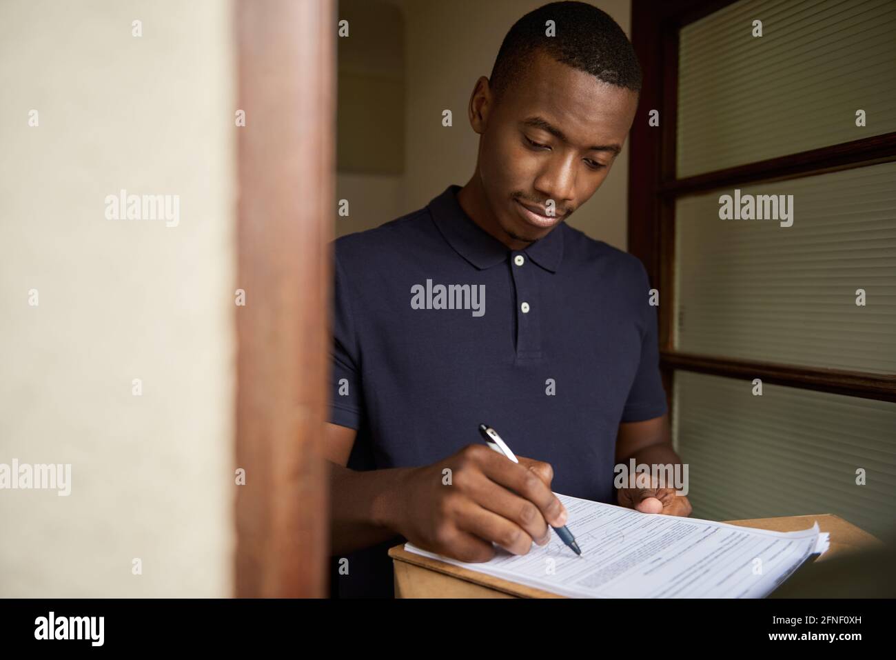 Young African man signing a courier's clipboard for a delivery Stock Photo