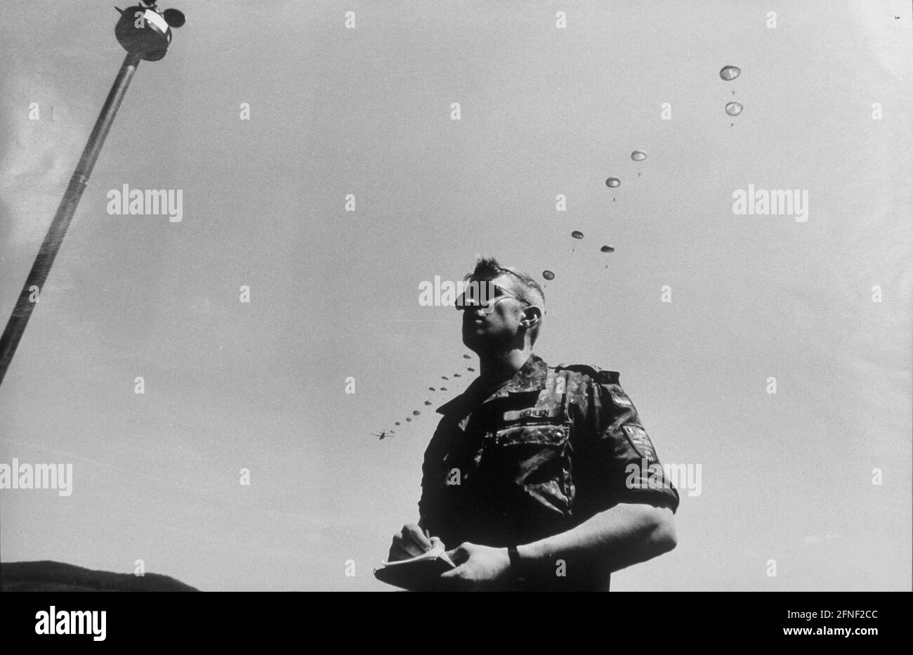 A paratrooper stands at the wind gauge on the Sennelager training area near Paderborn, while the parachutes of other jumpers can be seen above him. [automated translation] Stock Photo