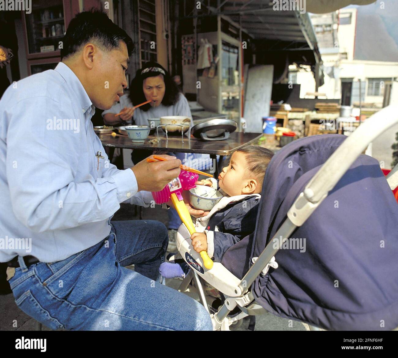 In a street-side restaurant on Lantau Island, a father feeds his son with chopsticks. [automated translation] Stock Photo