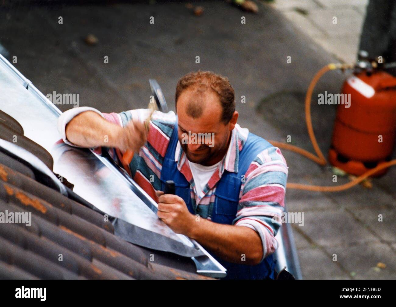 A roofer works on the roof of a house fixing roof shingles. [automated
