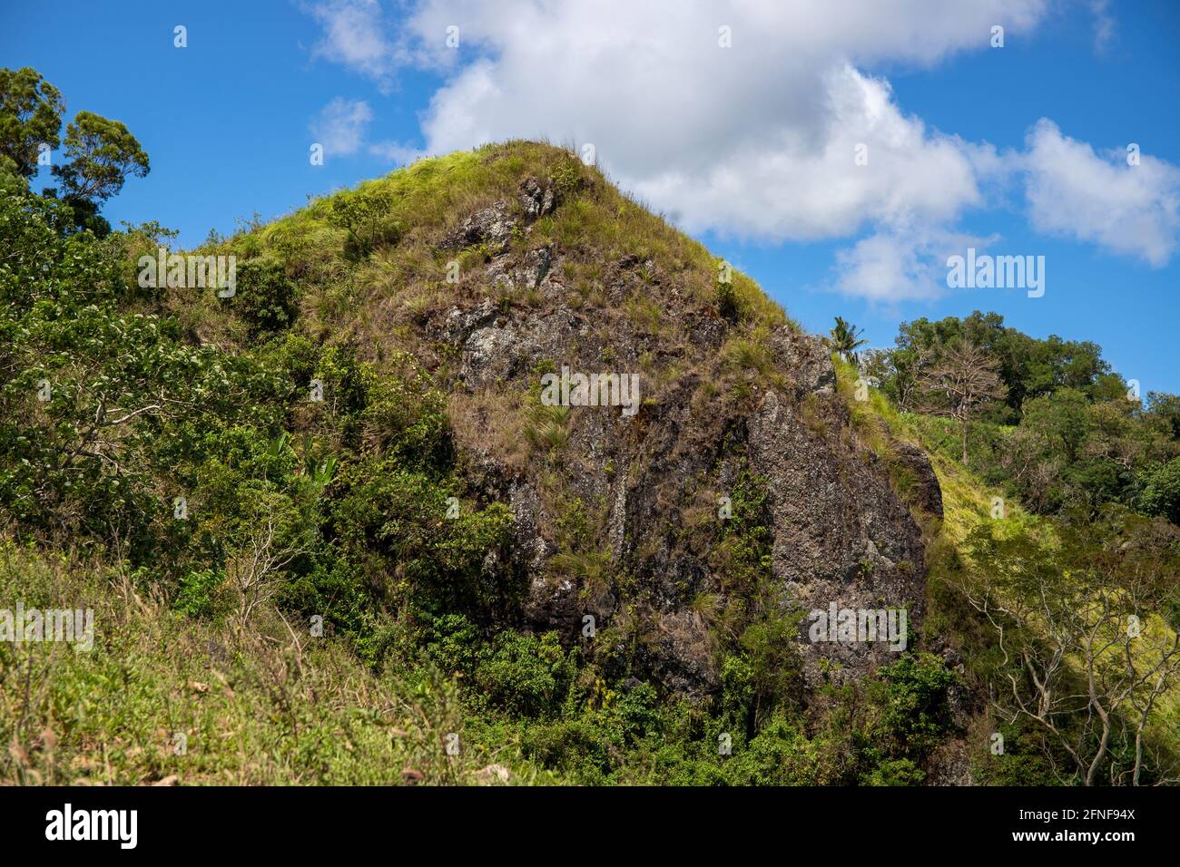 Green mountain rock peak under blue sky optimistic landscape. Rural land scenery. Summer travel hiking in green hills. Untouched nature parkland. Volc Stock Photo