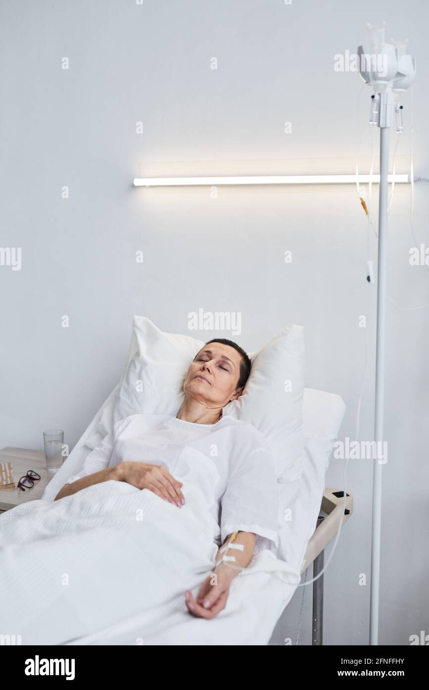 Sick mature woman lying on bed with her eyes closed under the drip at