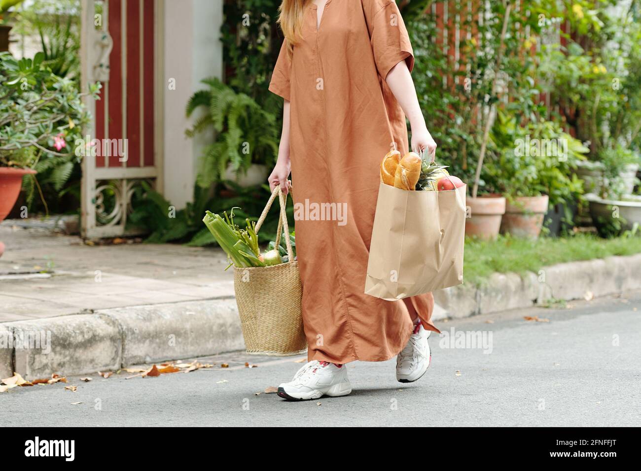 Cropped image of young woman carrying two bags full of groceries, bread