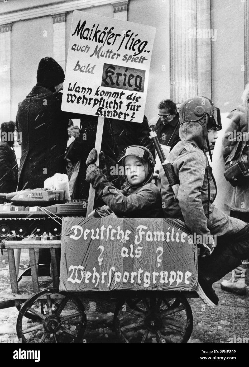 Two children dressed as soldiers protest at a demonstration of the peace  movement with posters such as ""German family as a military sports group""  and ""Maybug fly.... Mother will soon be playing