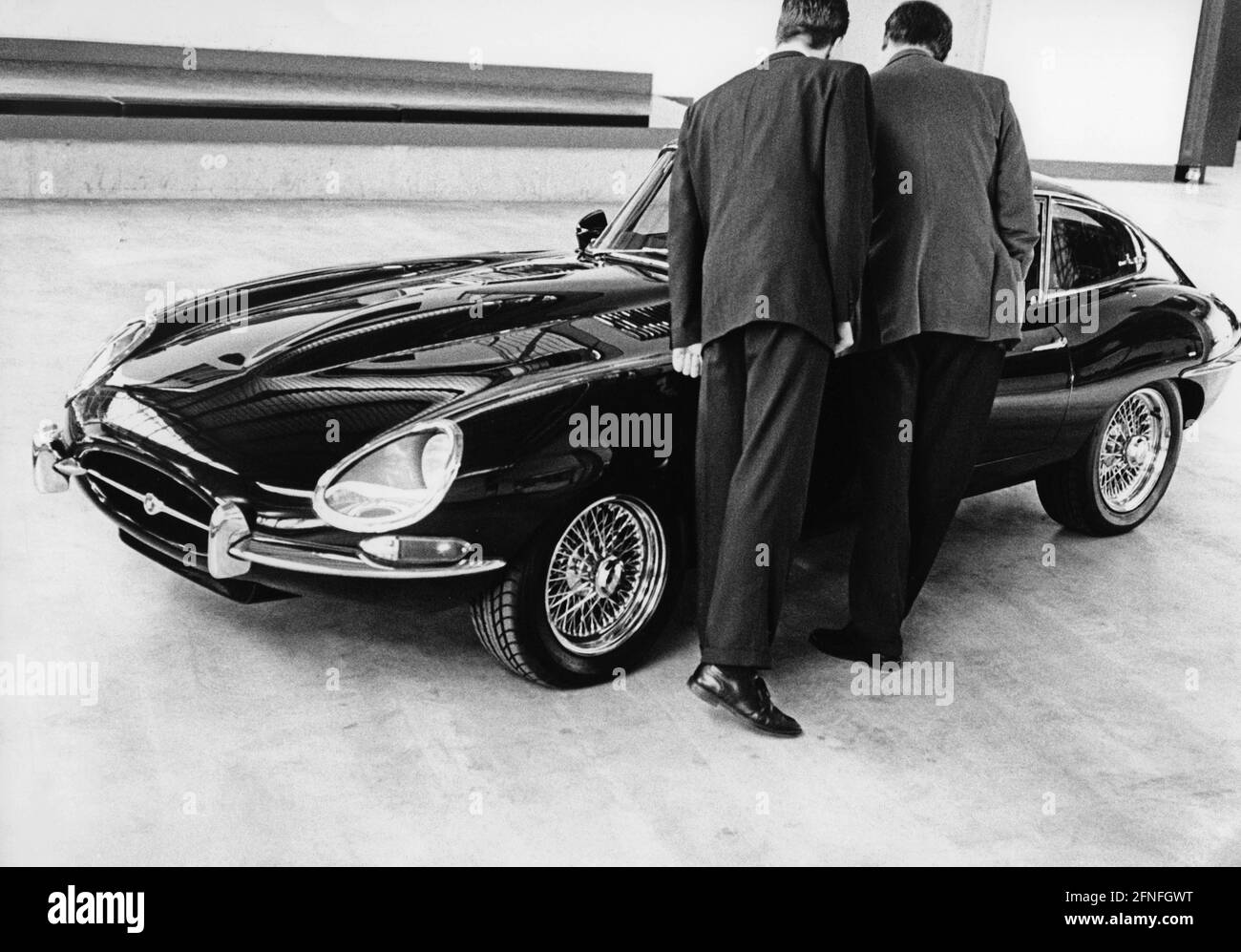 Two men look at a Jaguar E-Type Coupé (XK-E) of the first series. Today, the E-Type is a sought-after collector's item among classic car fans. A vehicle from the first series can be recognised by the Plexiglas covers over the headlights. [automated translation] Stock Photo