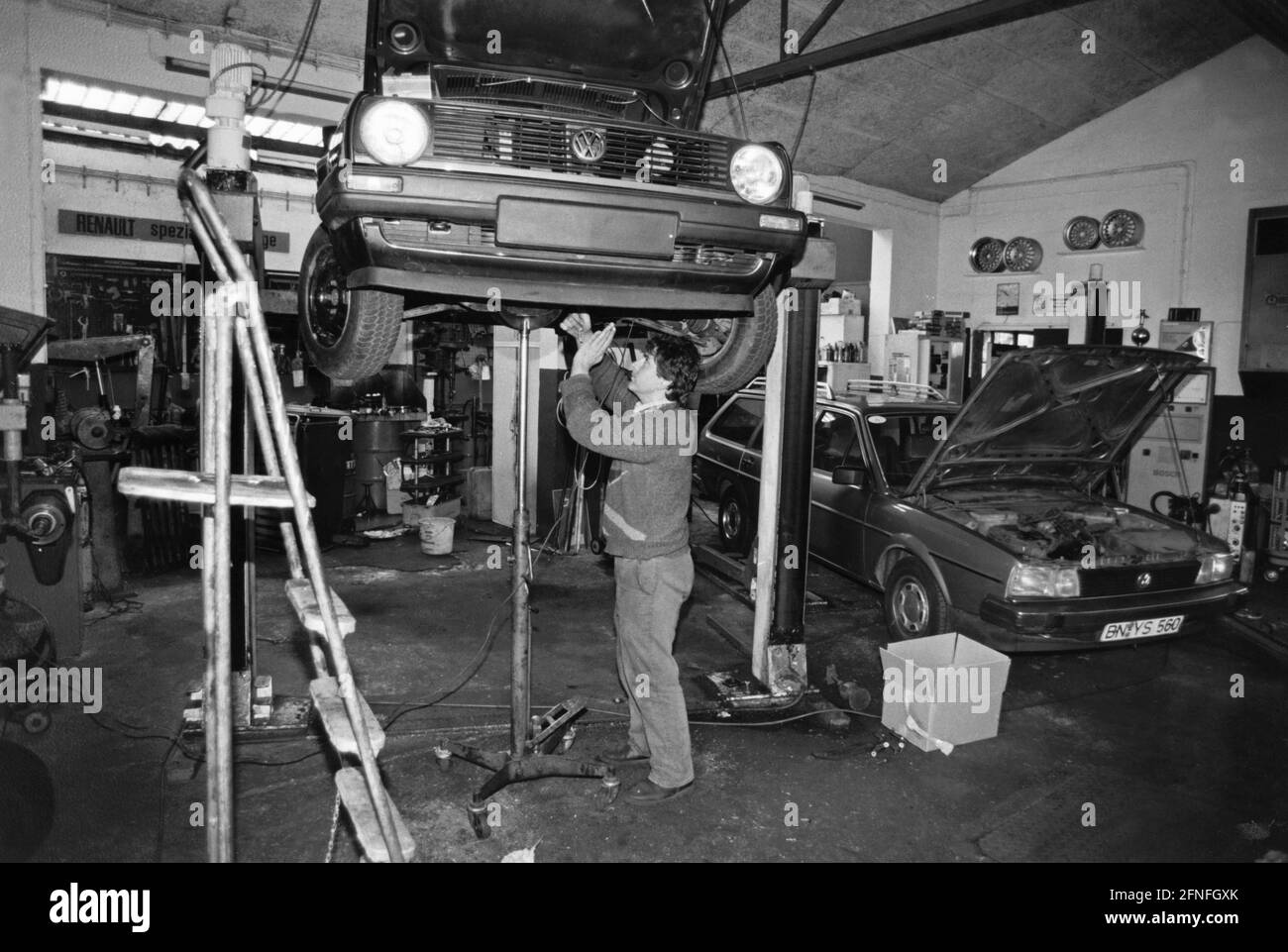 A self-employed master car mechanic in his workshop in Bonn. On the lifting platform of VW Golf II, next to it, with the bonnet open, a VW Passat B2. [automated translation] Stock Photo