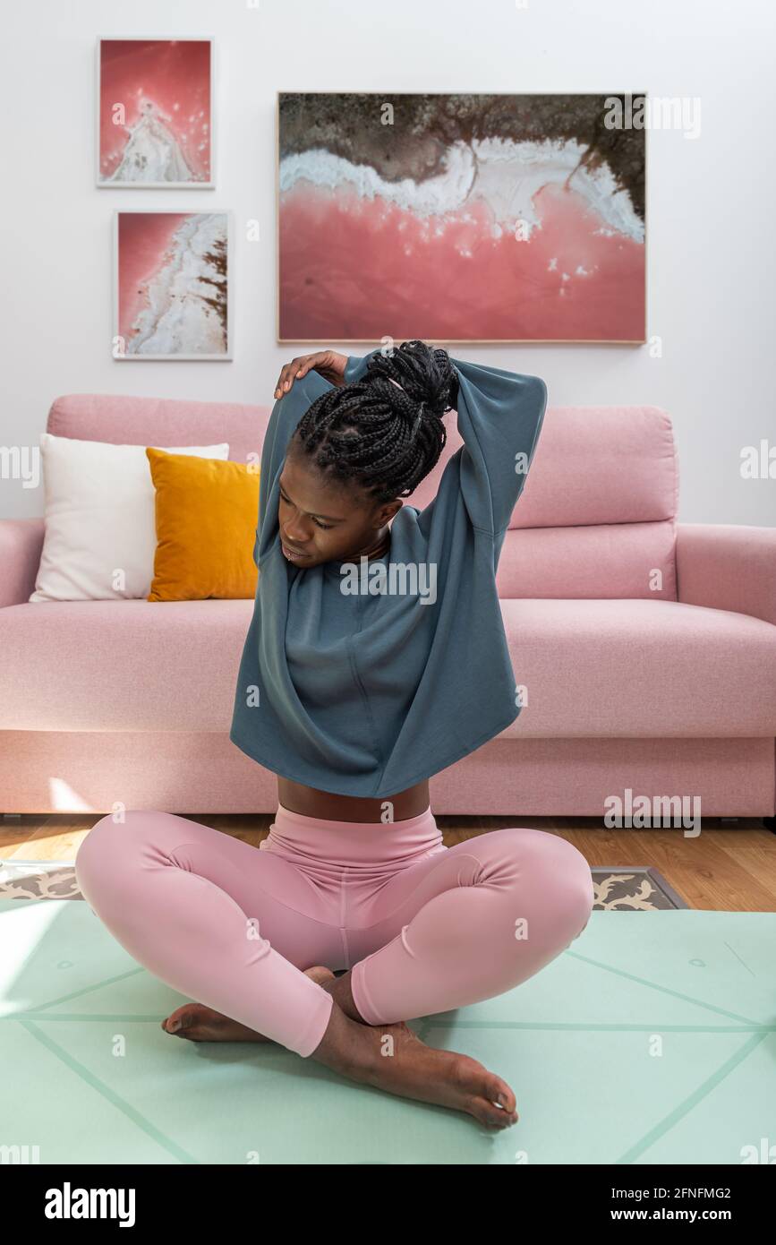 Fit African American female sitting on mat and stretching arms while warming up before workout at home Stock Photo