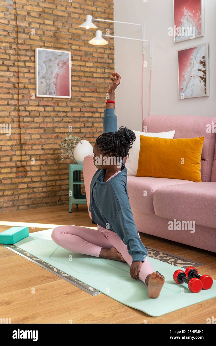 Black female in activewear stretching before workout at home while sitting on mat Stock Photo