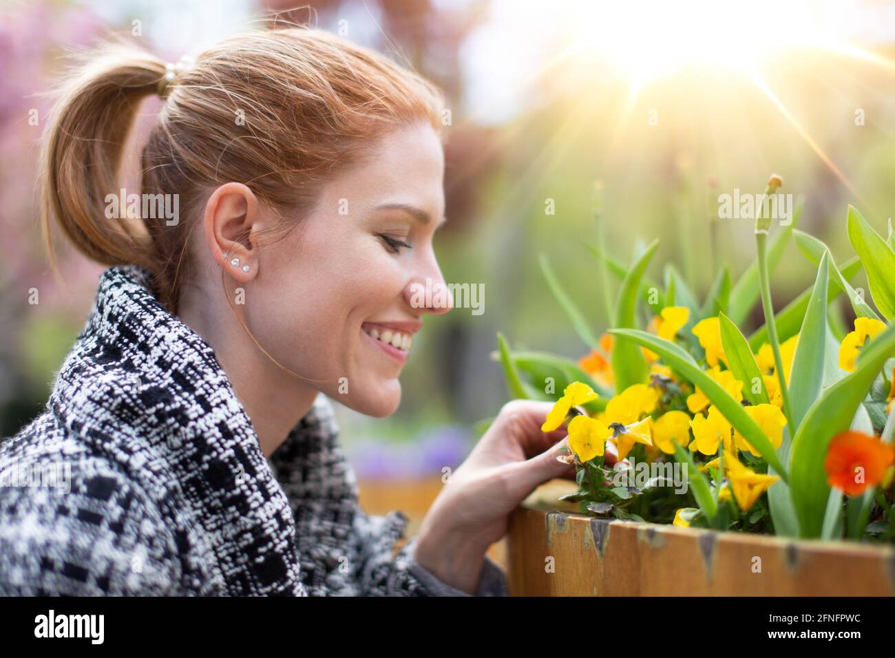 Happy young balanced Caucasian woman looking to flowers in park, profile view portrait Stock Photo