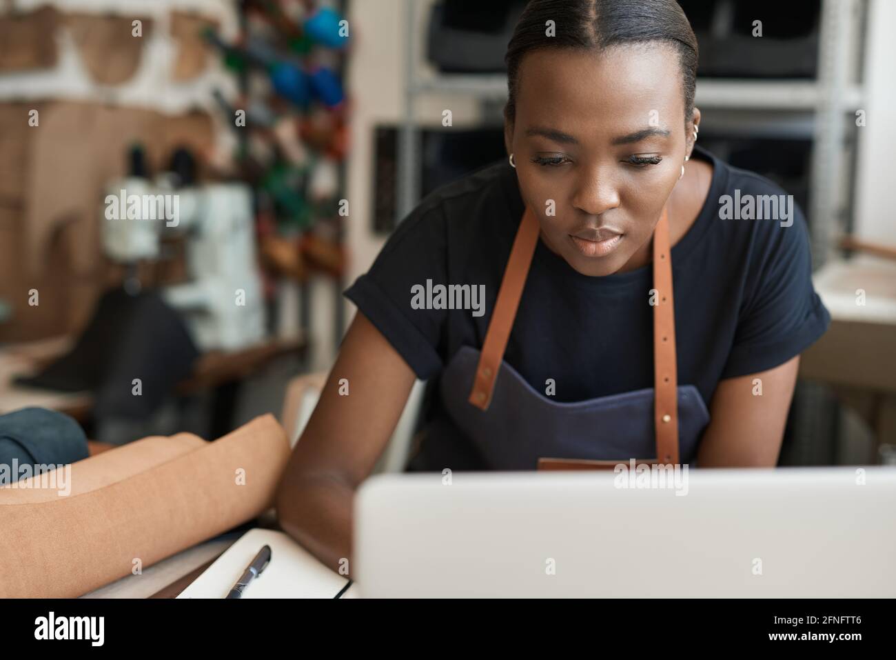 African female leather worker using a laptop in her workshop Stock Photo