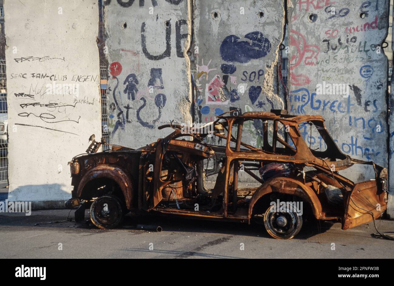 Burnt out Trabant in front of remains of the Berlin Wall. Photography around 1991 [automated translation] Stock Photo