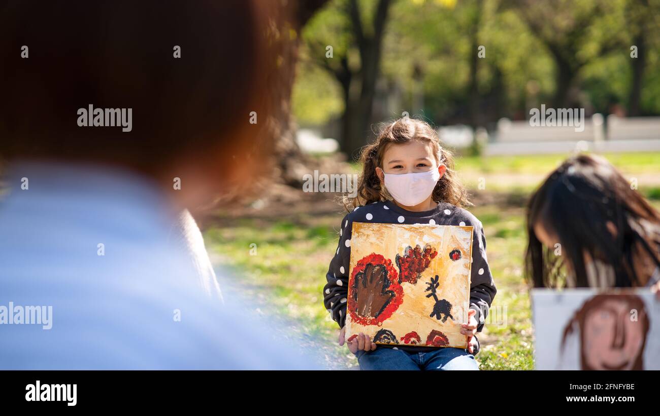 Small children with teacher outdoors in city park, learning group education and coronavirus concept. Stock Photo