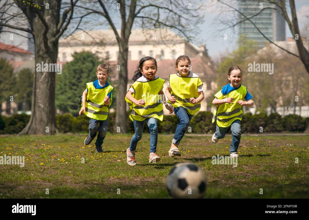 Small children playing football outdoors in city park, learning group education concept. Stock Photo