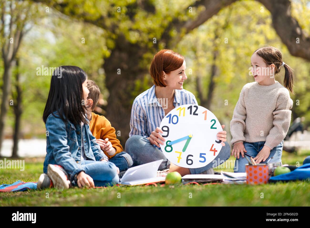 Teacher with small children sitting outdoors in city park, learning group education concept. Stock Photo