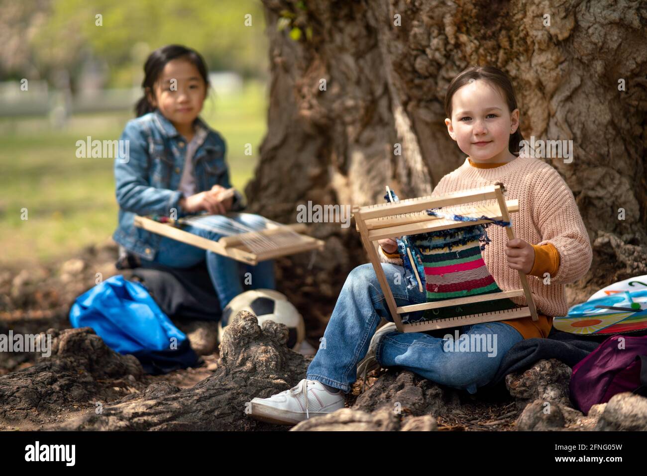 Small children with hand loom sitting outdoors in city park, learning group education concept. Stock Photo