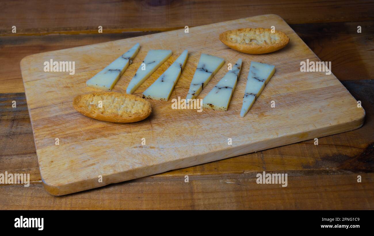 Cutting board with small triangular pieces of truffle cheese and thin ...