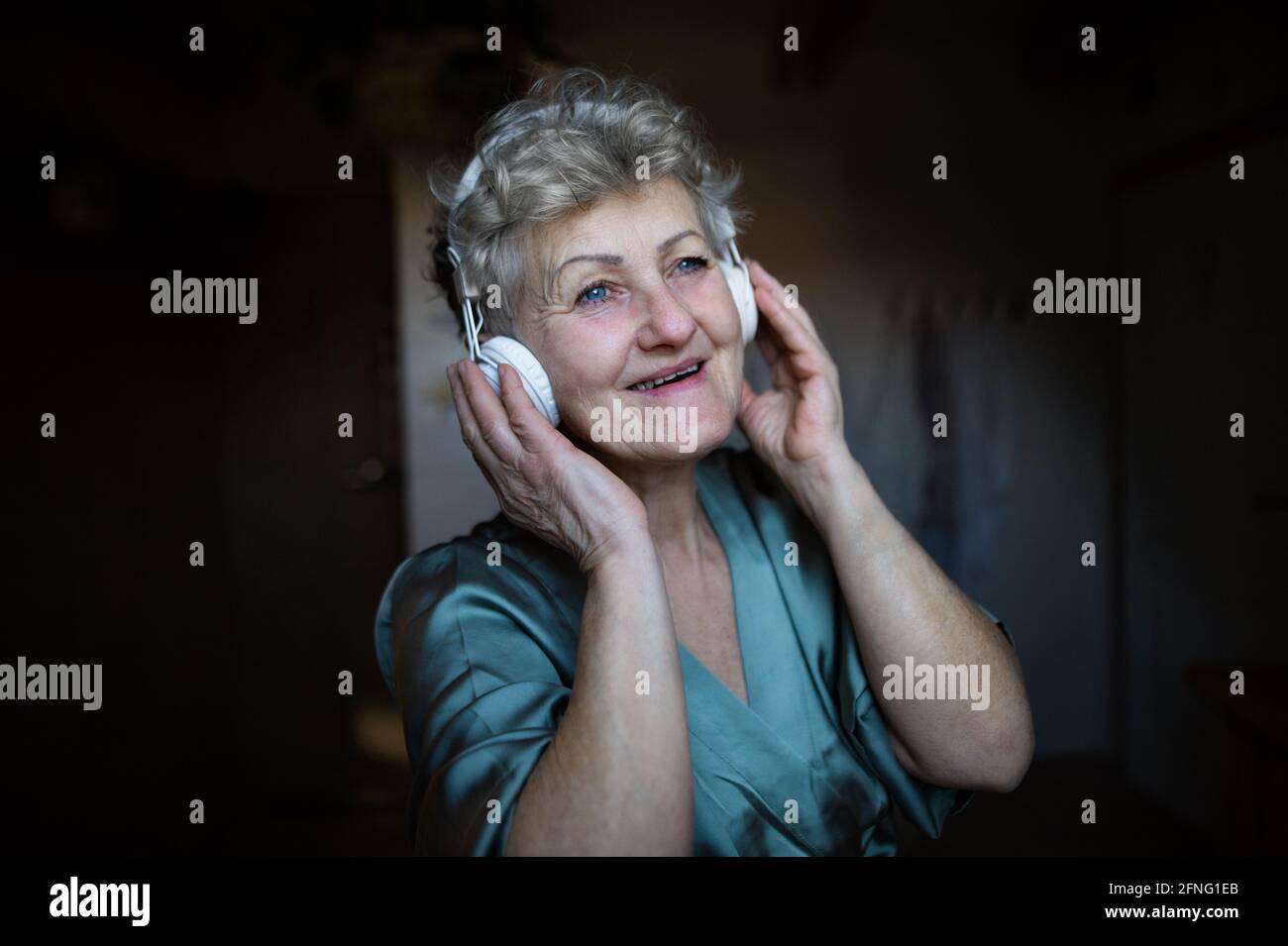 Happy senior woman with headphones listening to music at home, relax and self-care concept. Stock Photo