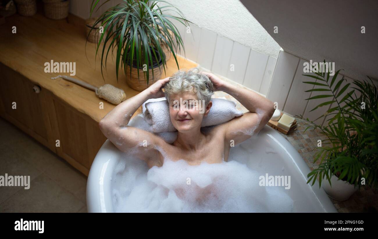 Top view of contented senior woman lying in bath tub at home, eyes closed. Stock Photo