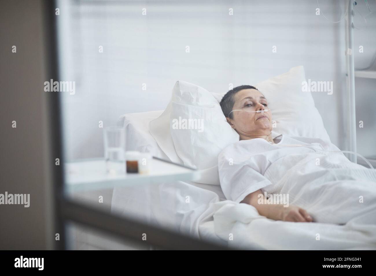 Mature woman lying on hospital bed under dropper at hospital Stock