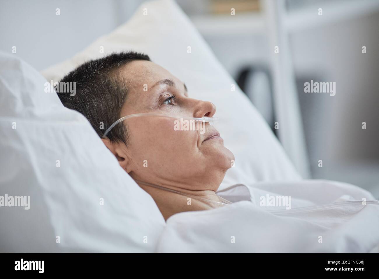 Side view of mature woman lying on hospital bed under dropper Stock