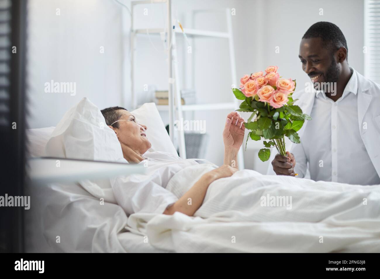 African man smiling and giving flowers to woman who lying on hospital