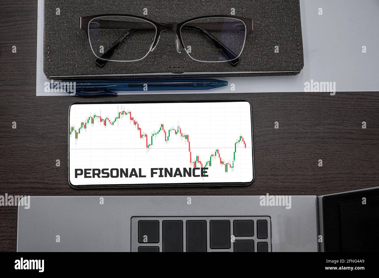 Personal finance concept. Top view of stocks price candlestick chart in phone on table near laptop, notepad and glasses with inscription. Business, fi Stock Photo