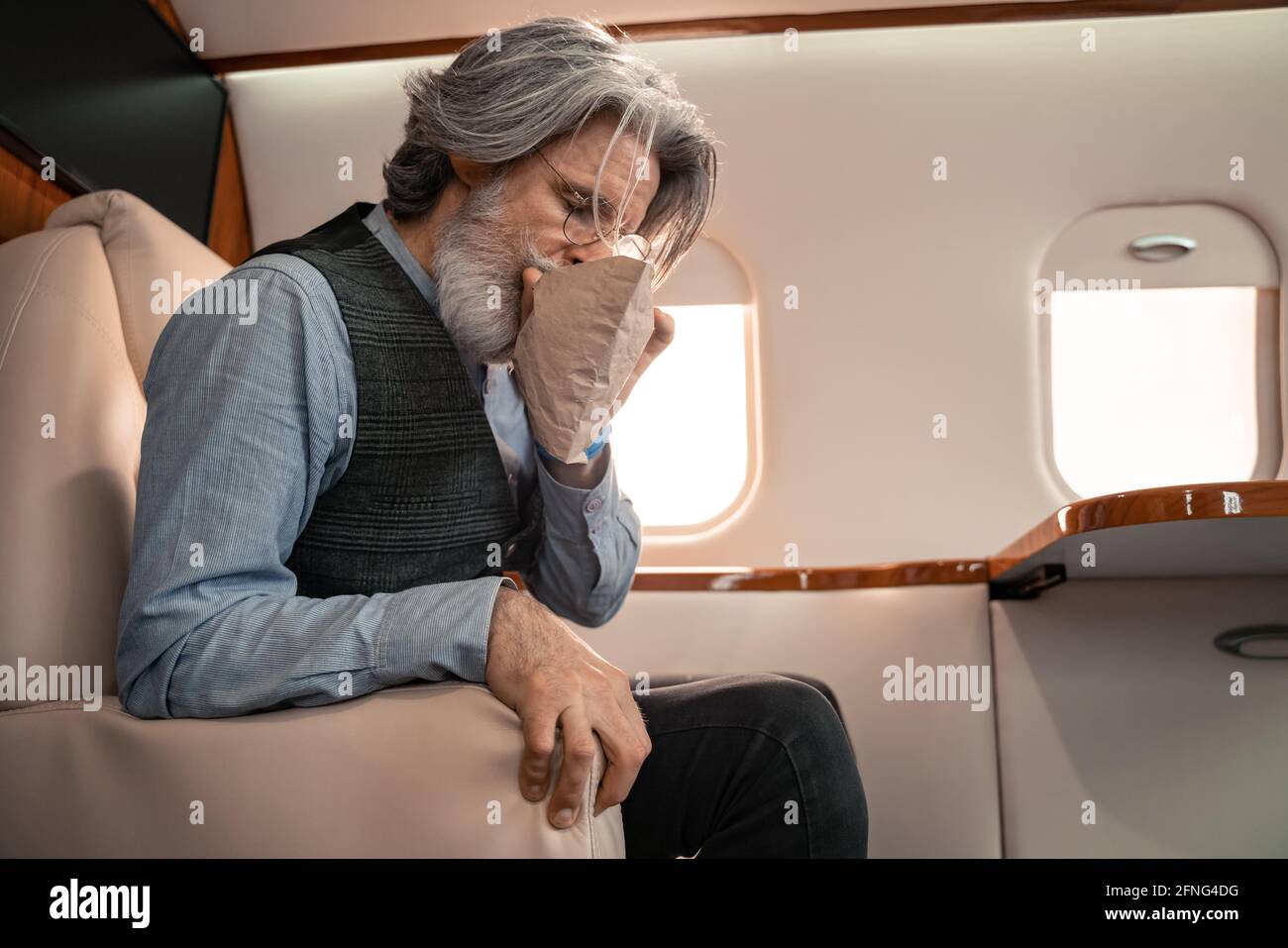 Mature man breathing in air sickness bag in private jet Stock Photo