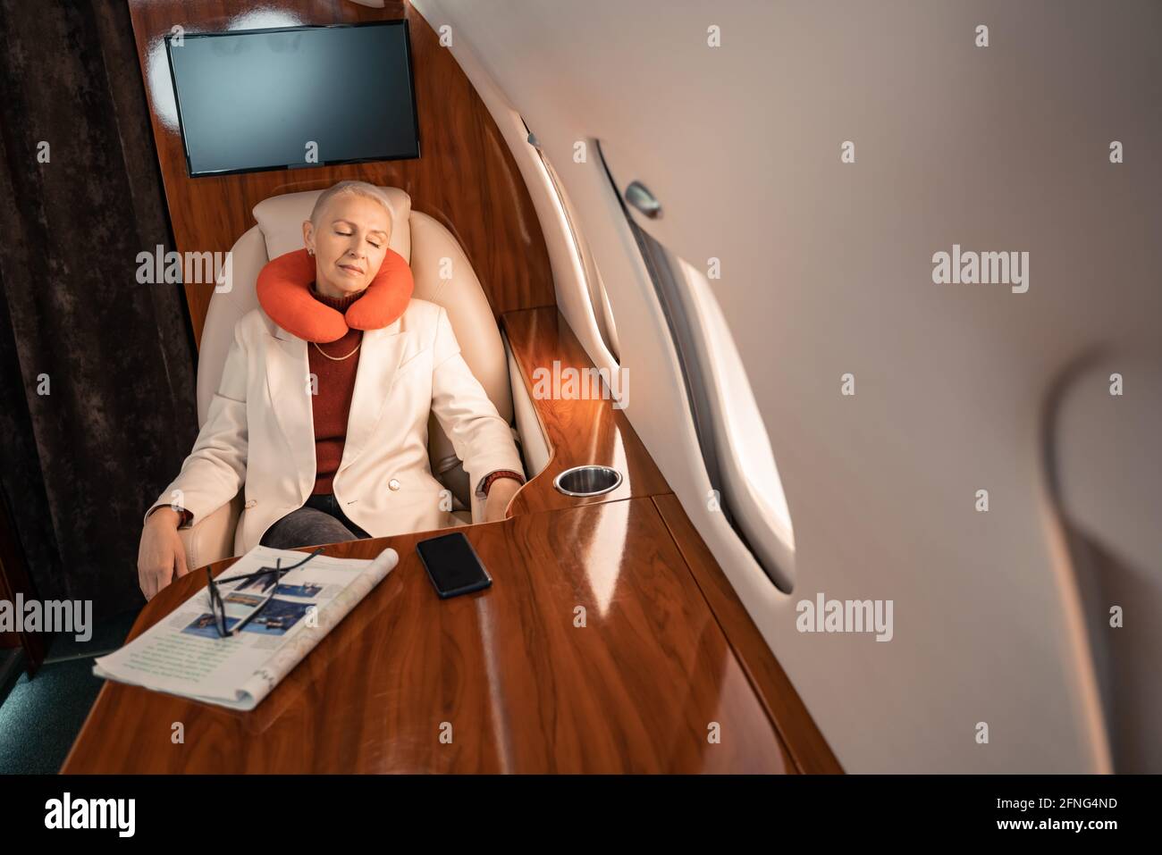Businesswoman in neck pillow sleeping near magazine and smartphone in