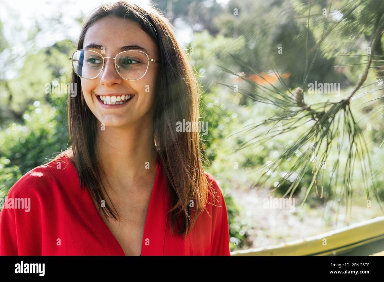 Young content female in eyewear and red clothes looking away on sunny day on blurred background Stock Photo