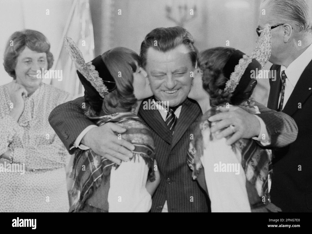 On his 65th birthday, Bavarian Prime Minister Franz Josef Strauß receives a kiss from Martina (left) and Erika, both wearing traditional dresses with headgear. Strauß' wife Marianne can be seen in the background on the left. [automated translation] Stock Photo