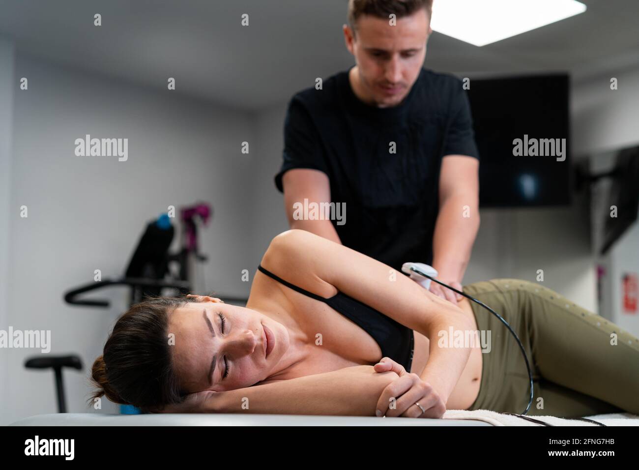Male physiotherapist applying laser to back skin of female during medical treatment in hospital Stock Photo