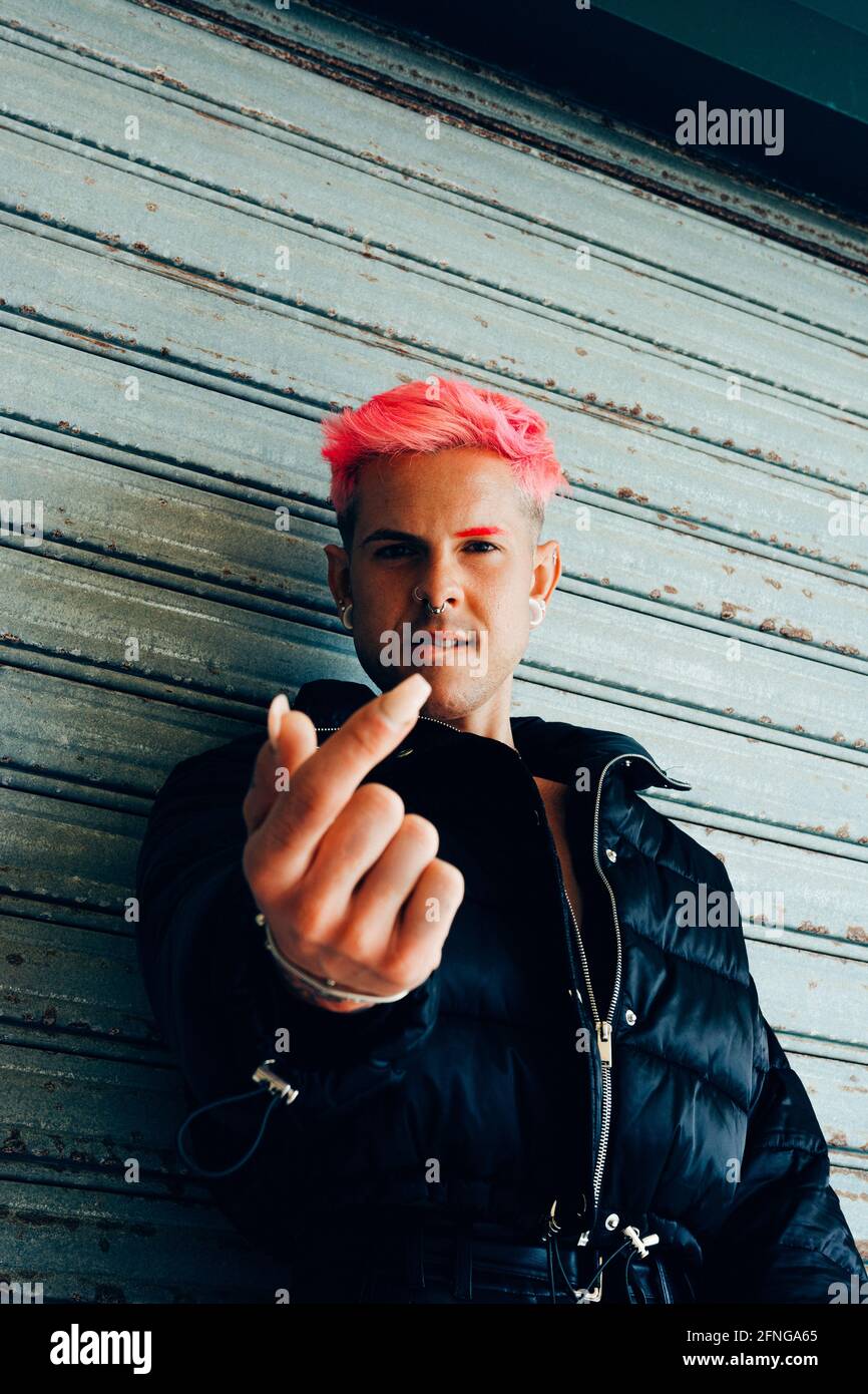 Trendy homosexual man in padded jacket with pink hair showing nail while looking at camera Stock Photo