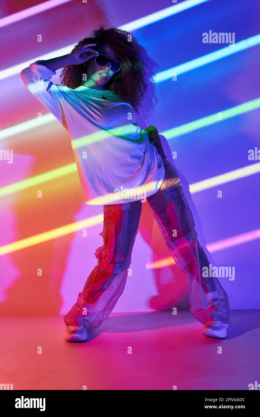 Full body stylish confident female dancer standing in neon lights and  touching sunglasses in dancing studio Stock Photo - Alamy
