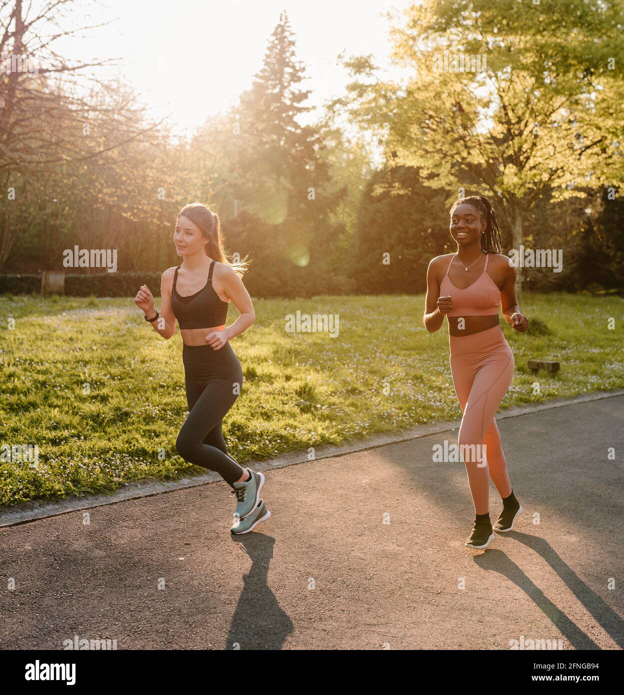 Smiling multiracial female runners in activewear jogging and talking during cardio training on walkway in town Stock Photo