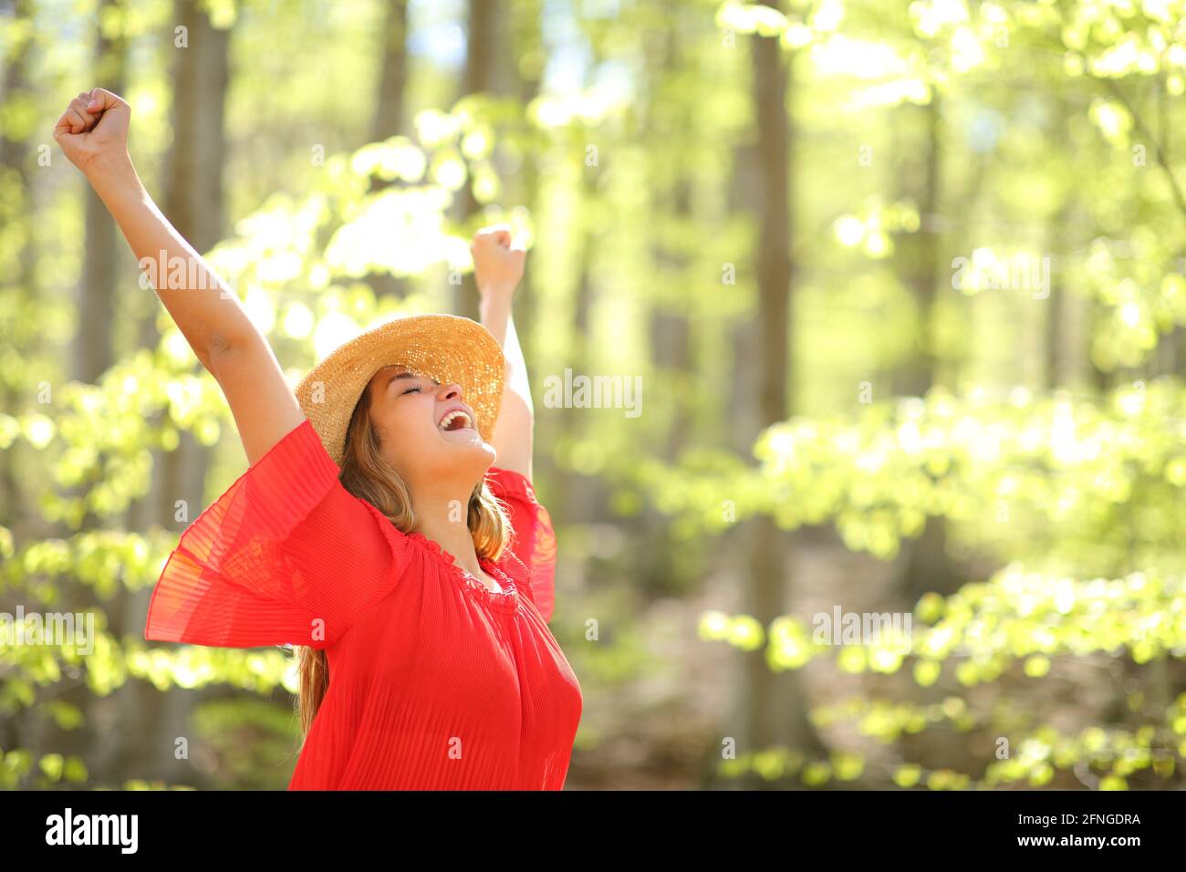 Excited woman in red celebrating vacation raising arms in a forest ...
