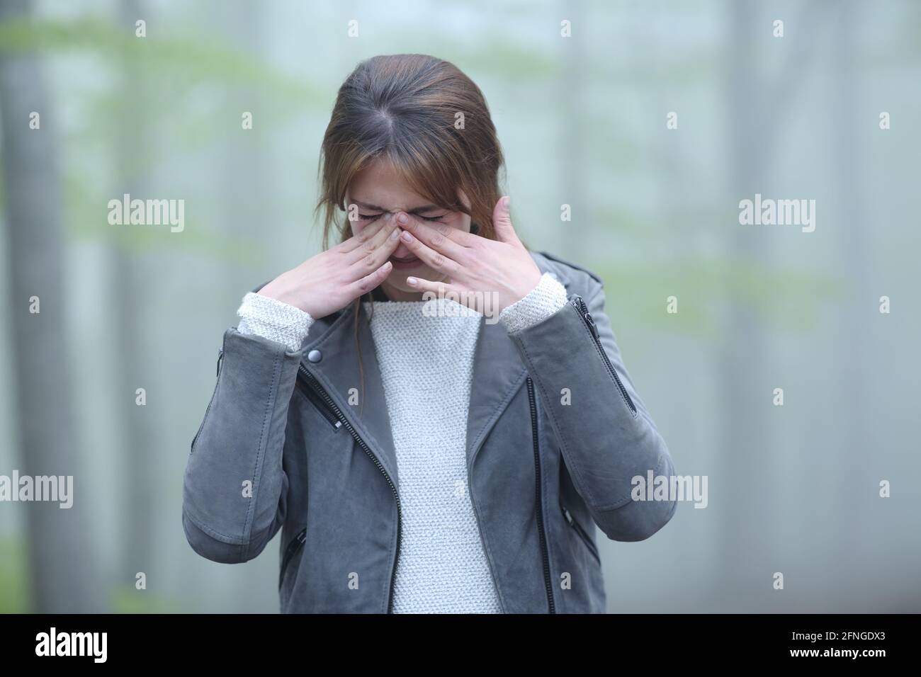 Front view of a woman scratching itchy eyes in a foggy forest Stock Photo