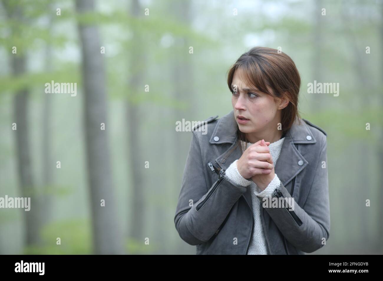 Scared woman walking alone towards camera in a foggy forest Stock Photo