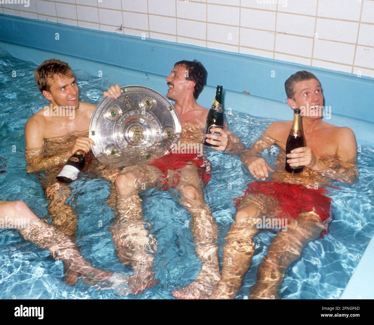 'FC Bayern München German Champion 1990. FC Bayern championship celebration in the dressing room. 12.05.1990. From left: Hans-Dieter ''Hansi'' Flick, Jürgen Kohler and Thomas Strunz with the championship trophy in the fatigue pool. [automated translation]' Stock Photo