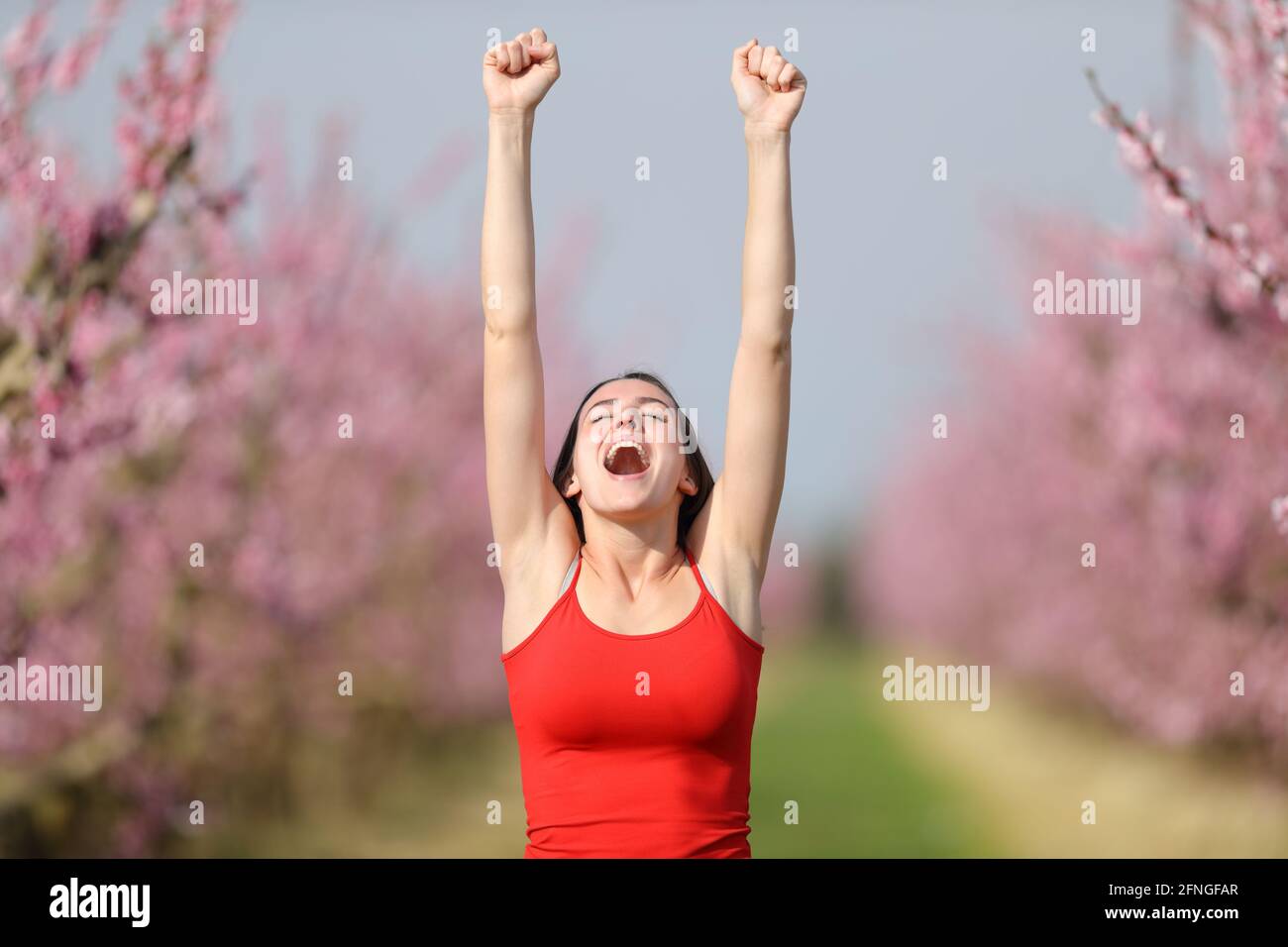 Front view of an excited woman in red raisng arms showing waxed armpit in nature Stock Photo