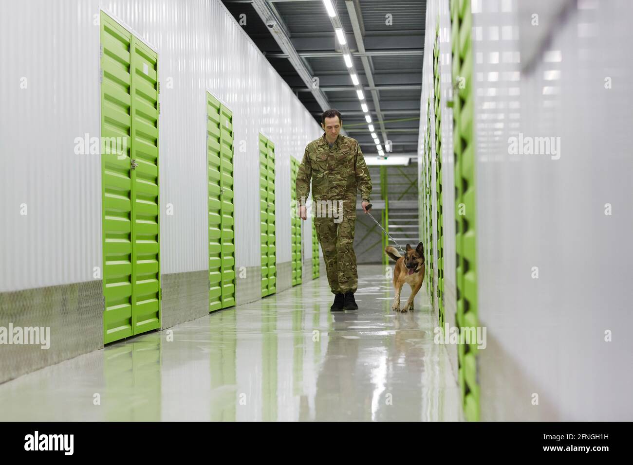 Young man in military uniform walking along the corridor with dog to check the warehouse Stock Photo