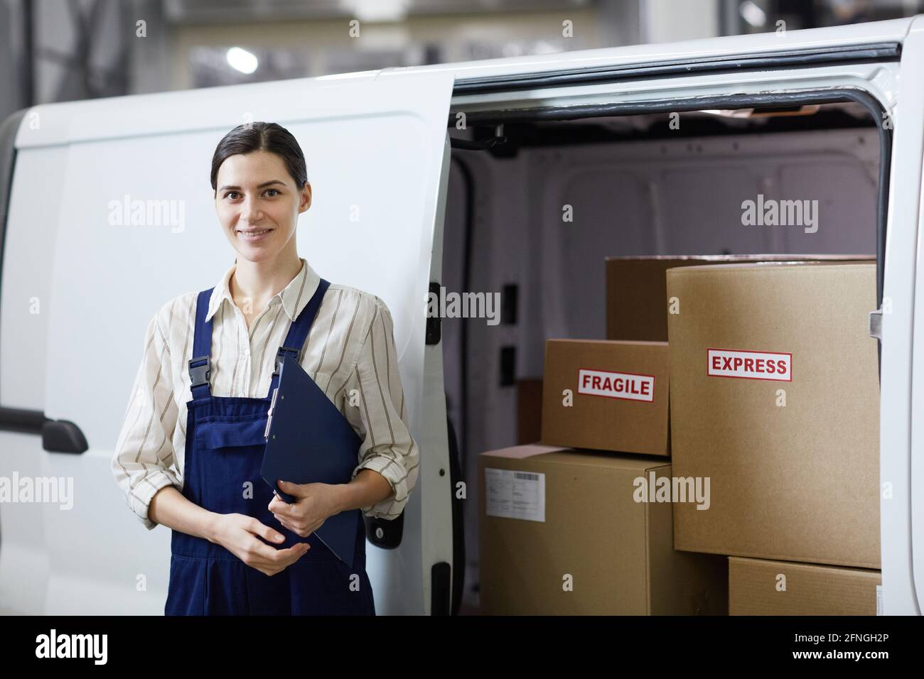 Portrait of young woman in uniform smiling at camera standing near the lorry she working in delivery service Stock Photo