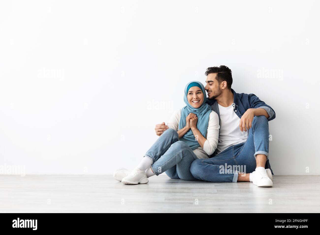 Joyful woman in hijab sitting on floor with her husband Stock Photo
