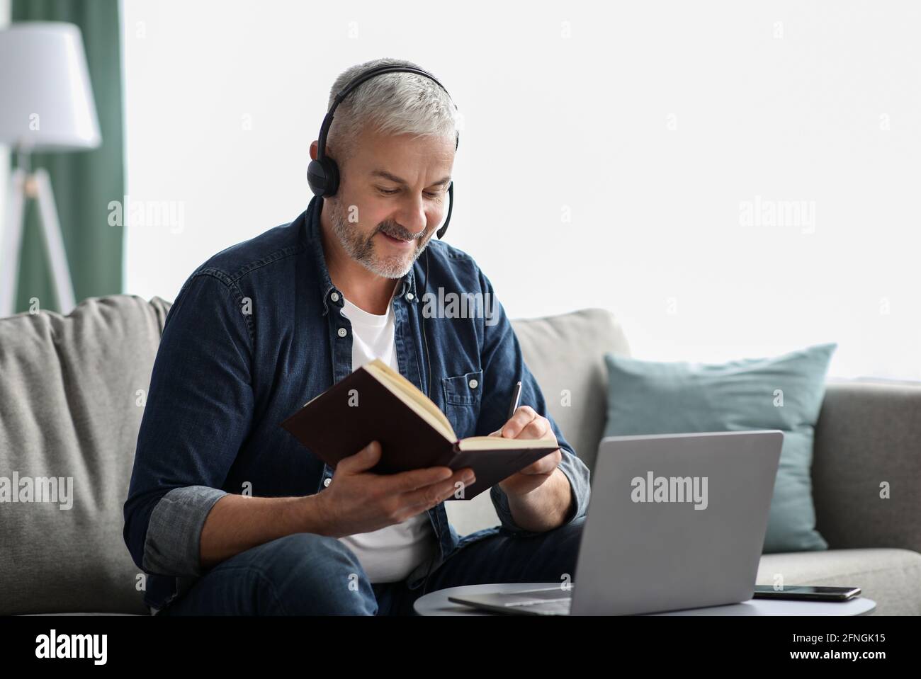 Happy old man having online class, using laptop and headset Stock Photo