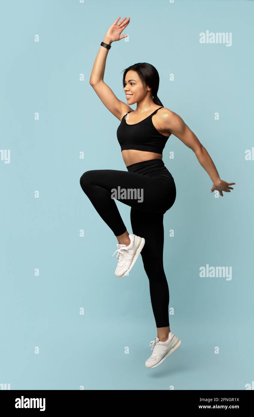 Sport concept. Young african american lady jumping, exercising and lifting leg up over blue background Stock Photo