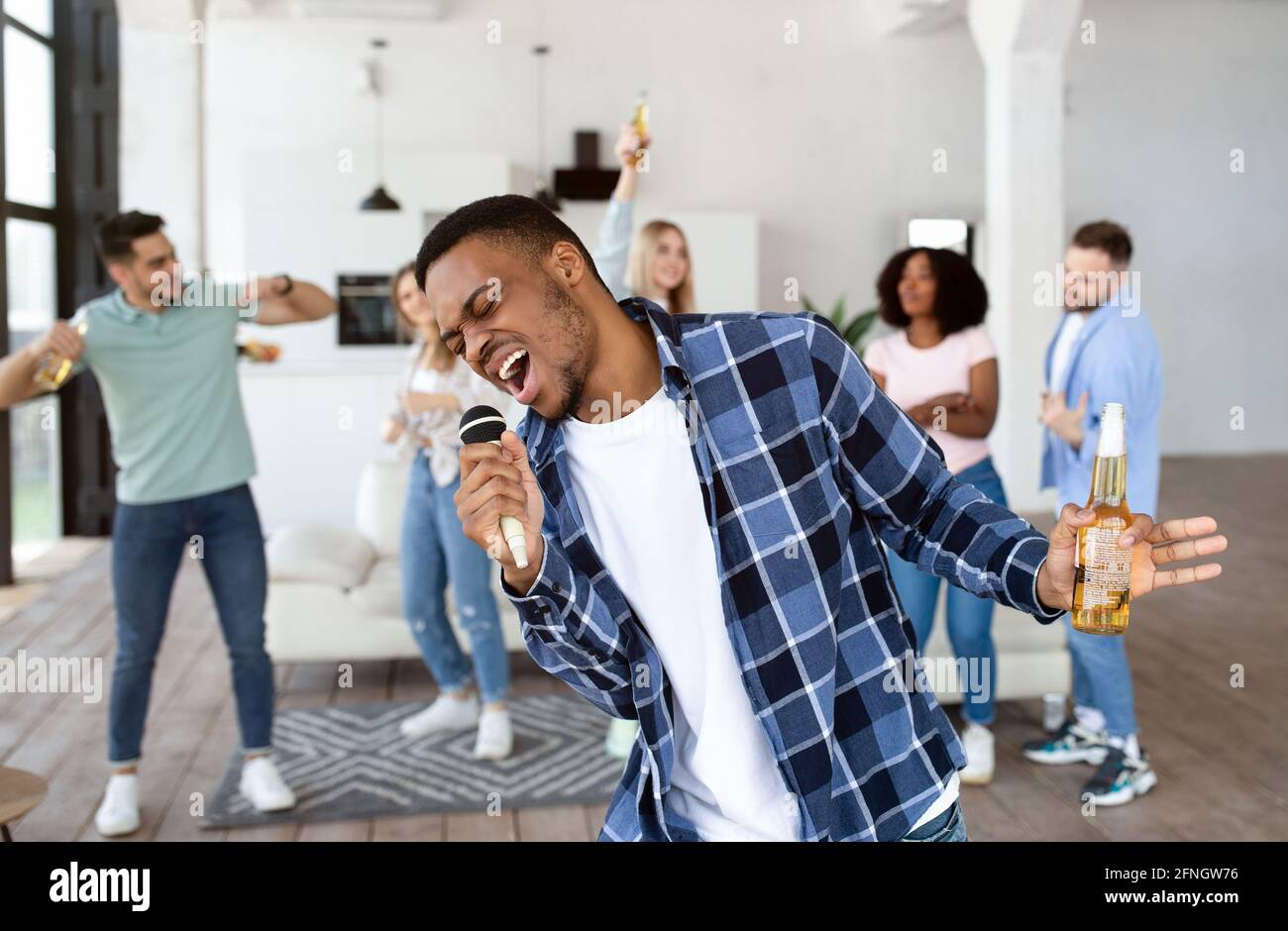 African American guy with beer bottle singing karaoke on home party