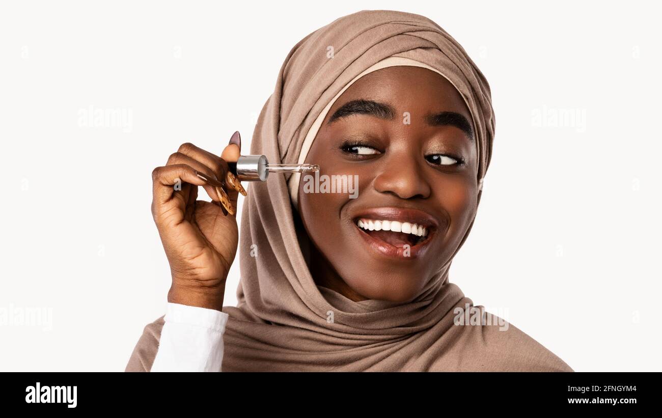 Muslim black woman applying moisturizer or hyaluronic acid on face Stock Photo