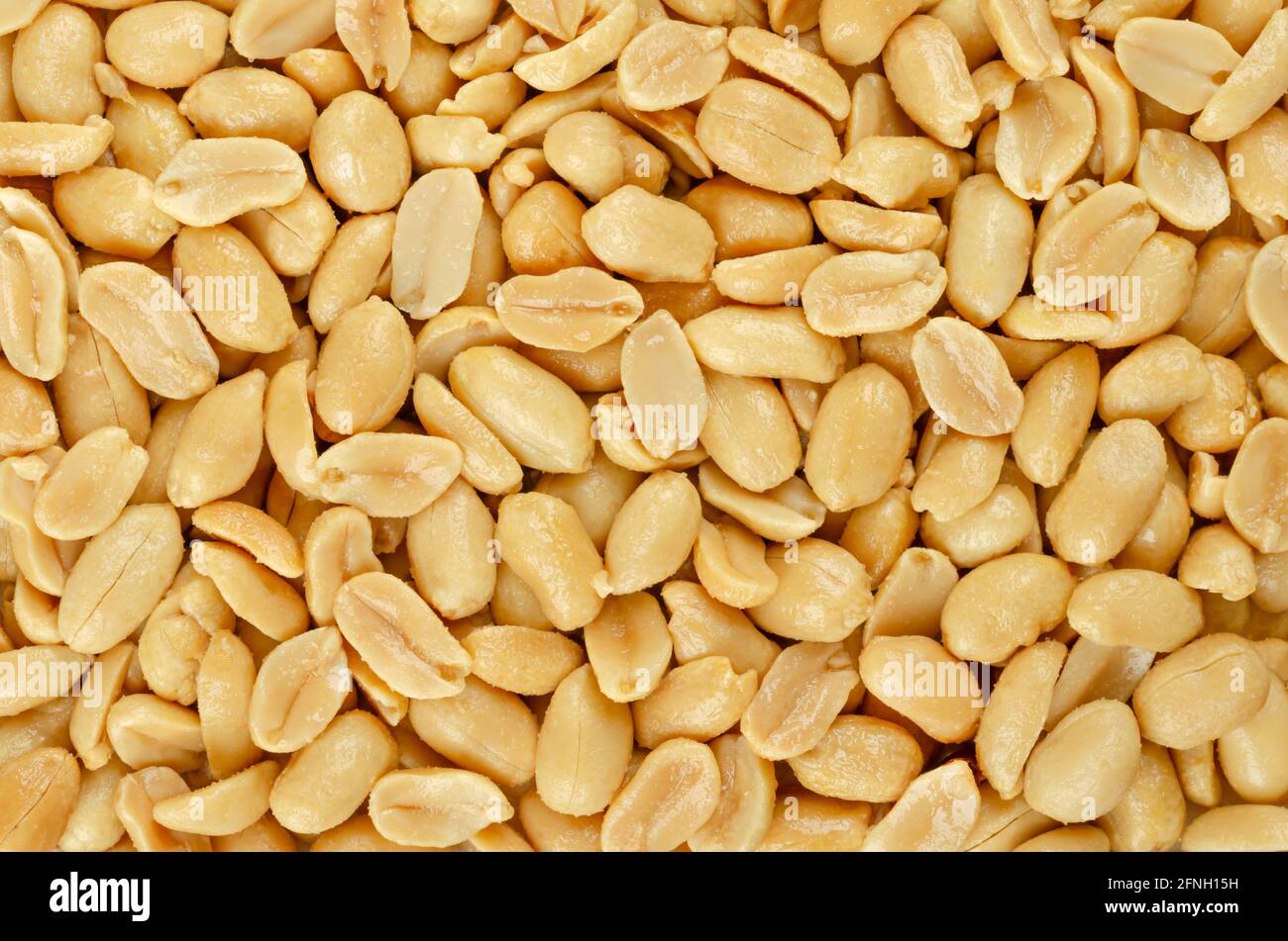 Roasted and salted peanuts, background, from above. Snack food, made from fruits of Arachis hypogaea, also groundnut, goober, pindar or monkey nut. Stock Photo