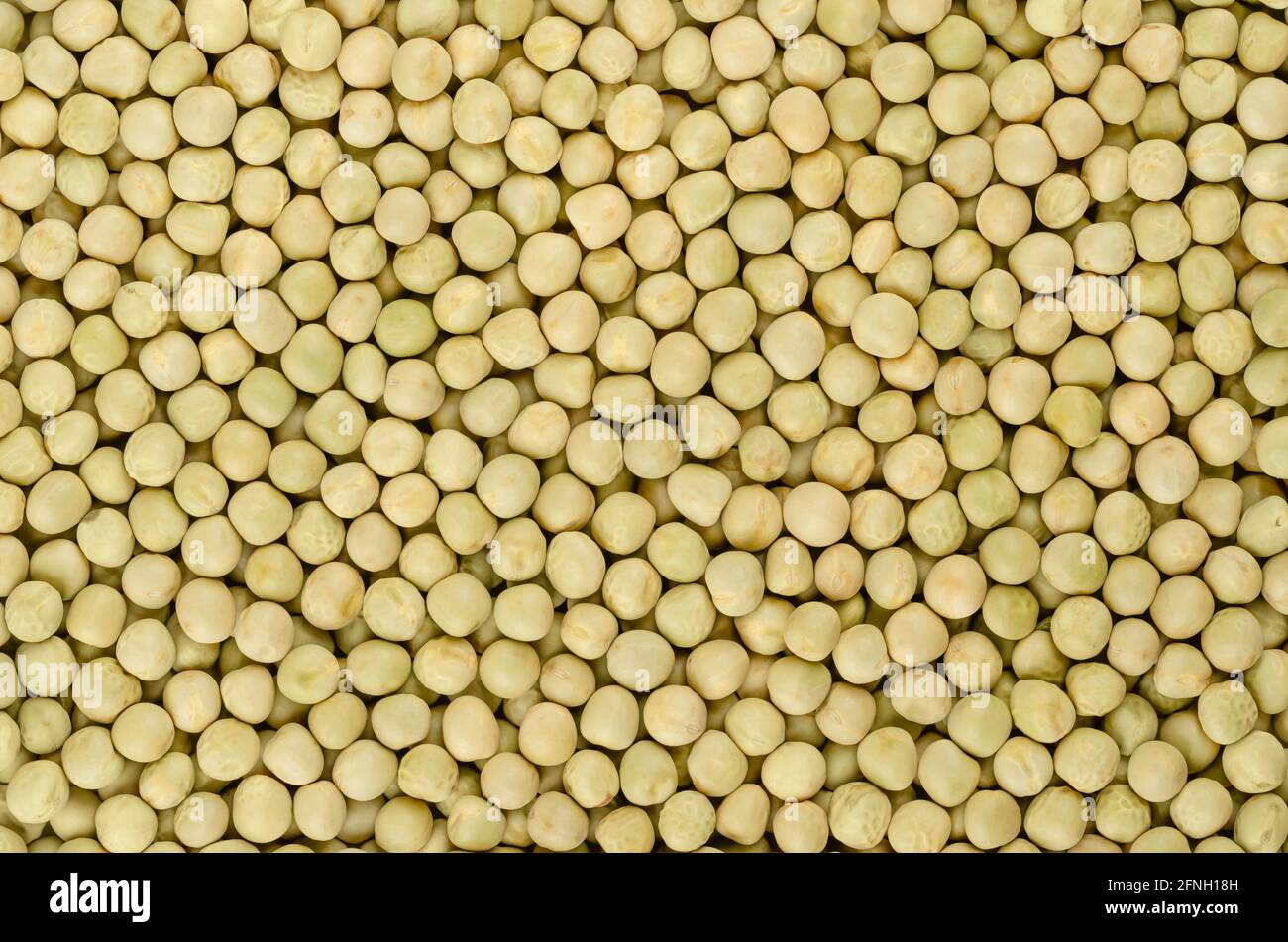 Dried whole peas, background, from above. Raw small spherical seeds of the pod fruit Pisum sativum with greenish and yellowish color. Stock Photo